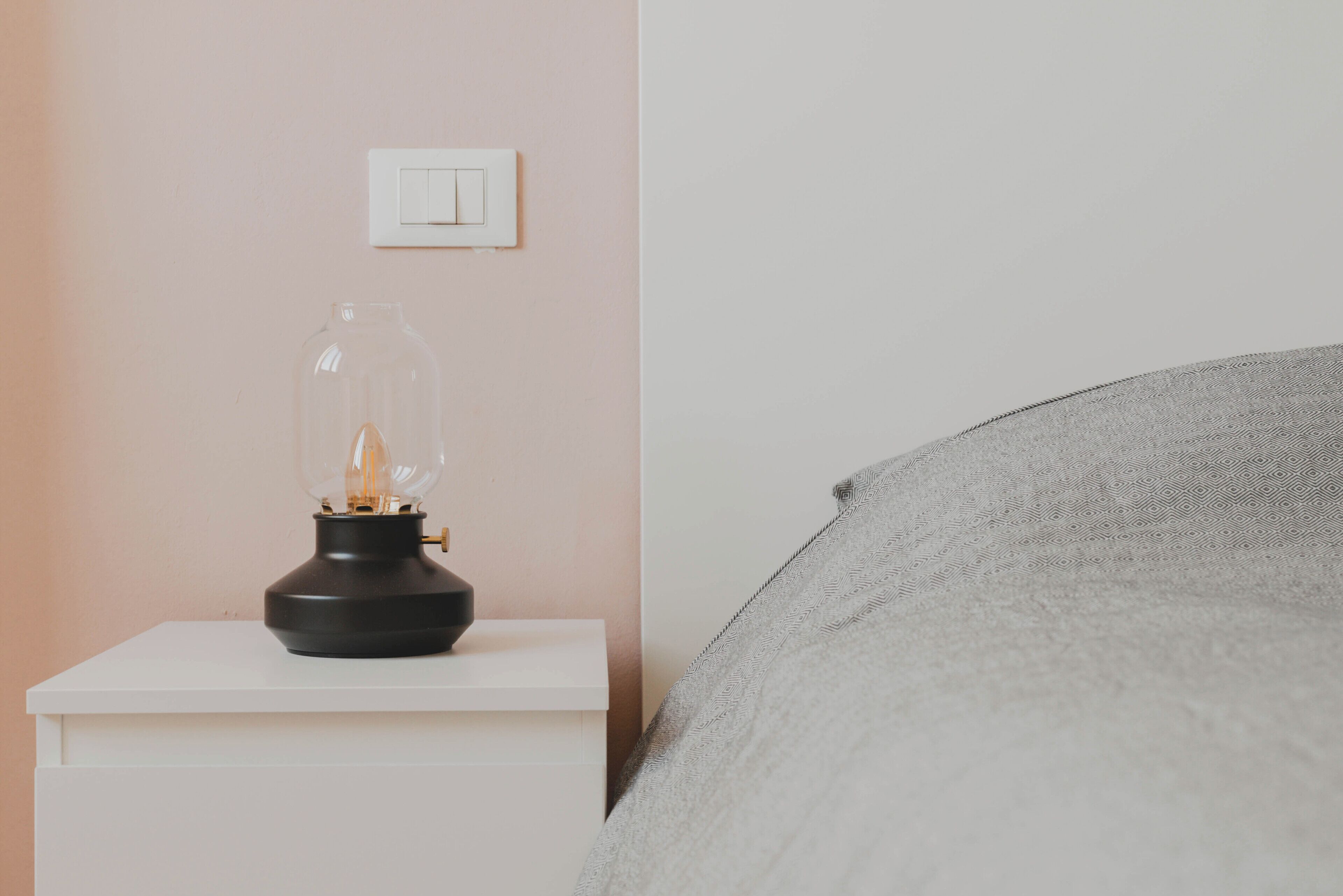 Una mesita de noche con una lámpara e interruptor en la pared.