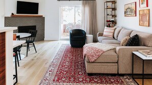 A modern living room with a fireplace, a sofa, a coffee table, and a dining area with chairs.