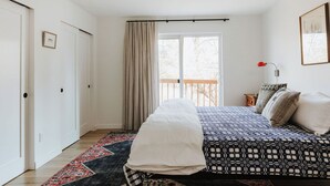 A bedroom with a bed, a window with curtains, a nightstand with a lamp, and a framed picture on the wall.