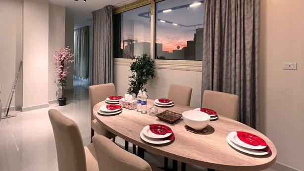 Un comedor moderno con una mesa redonda dispuesta para cuatro personas, con platos blancos y rojos, un bol central y una planta en maceta.