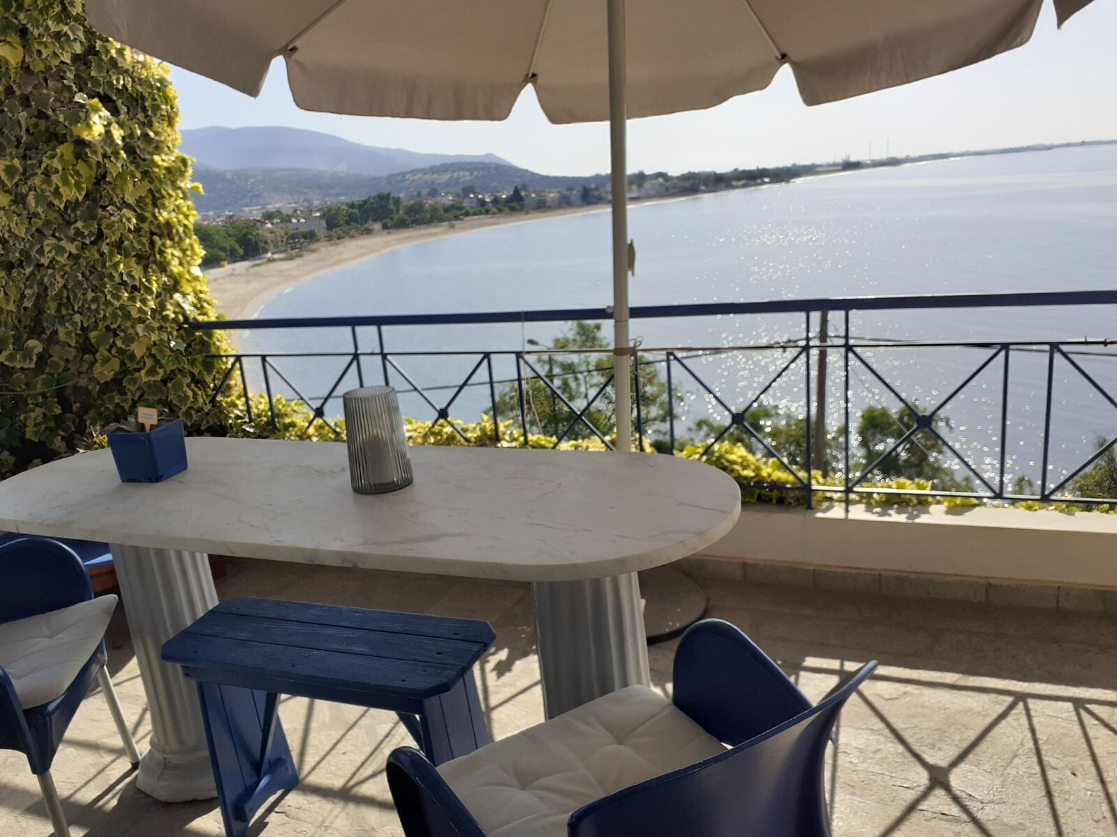 A terrace with a table and chairs, overlooking a body of water and a beach.