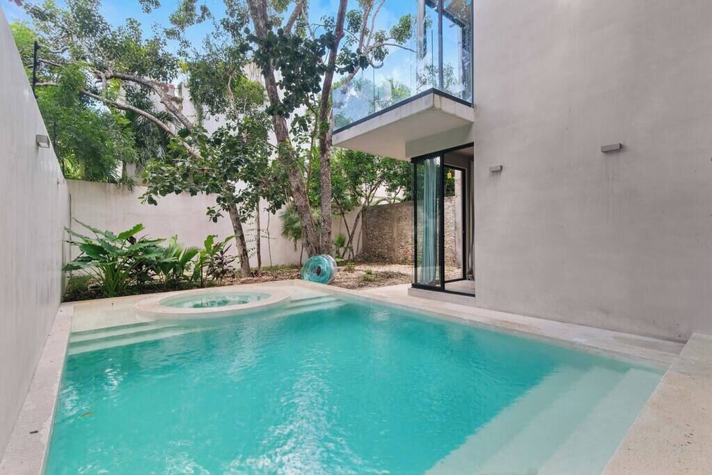 A swimming pool with a glass-enclosed deck, surrounded by trees and a concrete wall.