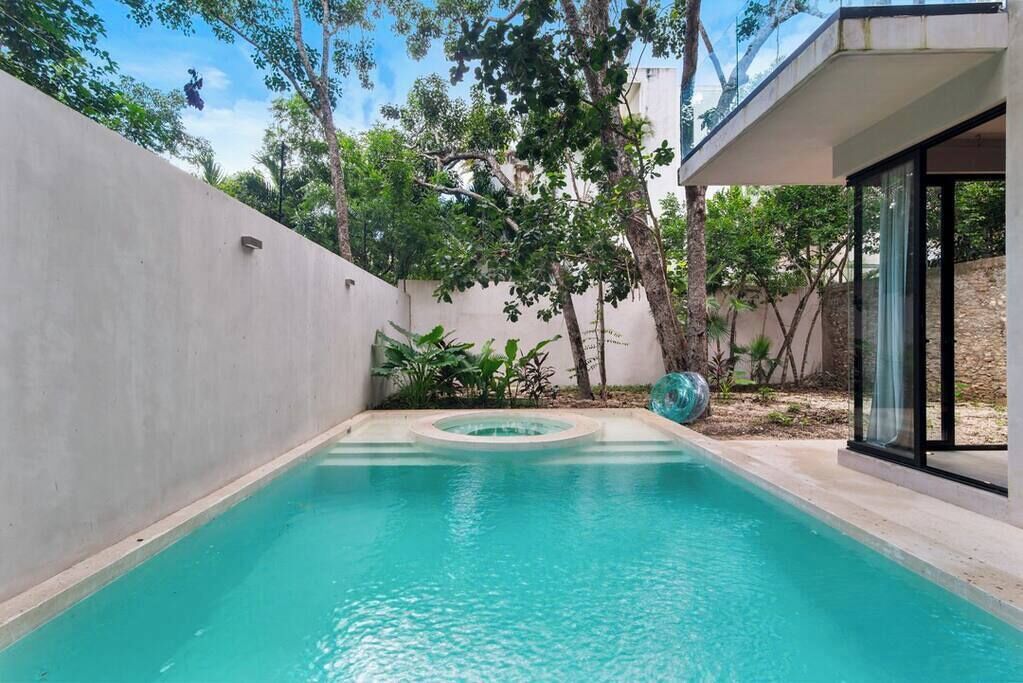 Une piscine avec un jacuzzi circulaire, entourée de verdure et bordée d’un bâtiment moderne.