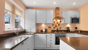 A modern kitchen with white cabinets, a granite countertop, a stainless steel range hood, and a built-in oven.