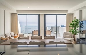 Amplia sala de estar con una gran mesa y sillas, un sofá y un amplio ventanal con vistas al mar.