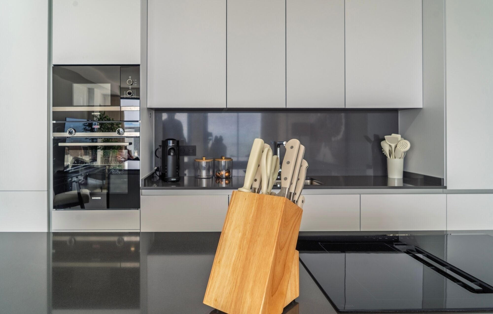 A modern kitchen with a built-in oven, a coffee maker, and a knife block on the countertop.