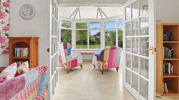 Una habitación con un amplio ventanal, dos sillones con tapicería colorida, una estantería de madera y un reloj de pared.