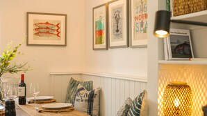 A dining area with a wooden table set for two, a wine bottle, and glasses. There are framed artworks on the wall above the table. - Cherry Tree House- North East Escapes (Amble)