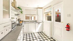 A modern kitchen with white cabinets, a black and white checkered floor, and a fire extinguisher mounted on the wall. - Cherry Tree House- North East Escapes (Amble)