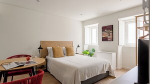Une chambre moderne avec un lit, un bureau et une chaise. Une fenêtre laisse entrer la lumière naturelle et une plante est posée sur la table de chevet.