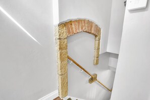 Un coin de pièce avec un mur blanc, une arche en briques et un balai en bois appuyé contre le mur.