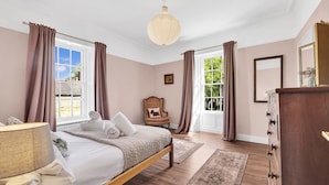 Een slaapkamer met een bed, een stoel, een dressoir en een raam met gordijnen.