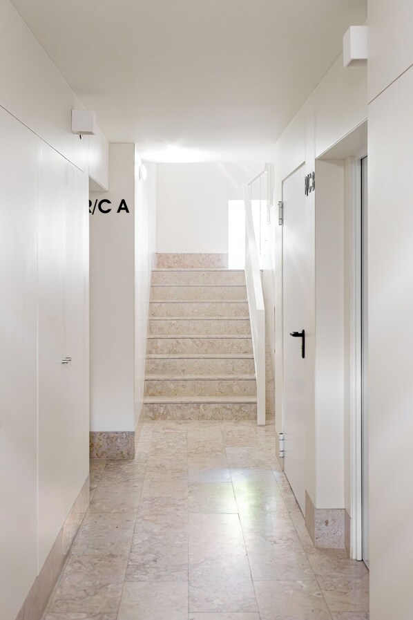 Un pasillo moderno de hotel con una escalera de mármol, paredes blancas y puertas numeradas.