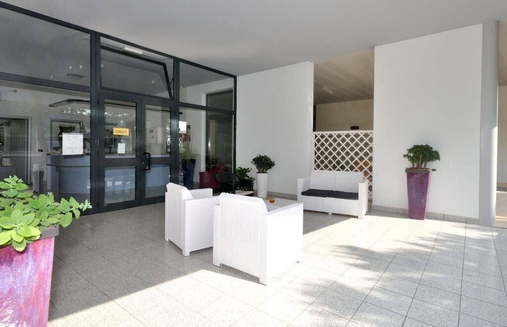 Un espace extérieur aménagé avec des meubles en osier blanc, des plantes en pot et une entrée avec une porte en verre.