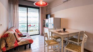 A compact living space with a sofa, dining table, chairs, a television, and a sliding glass door leading to an outdoor area.