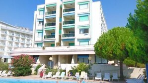 A hotel with a swimming pool, multiple balconies, and a clear blue sky.