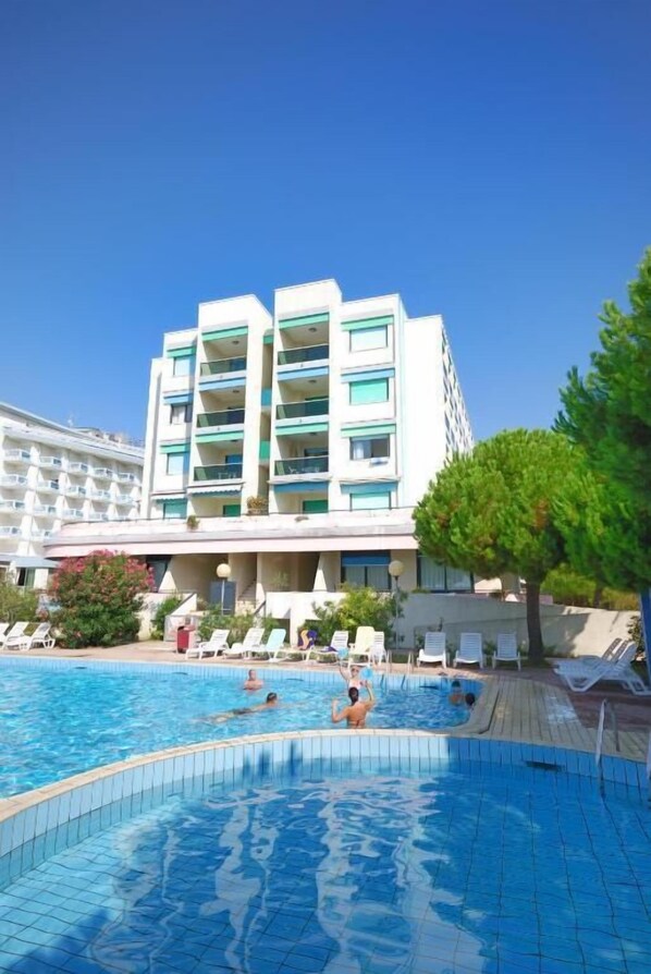 Ein Hotel mit Schwimmbad, mehreren Balkonen und blauem Himmel.