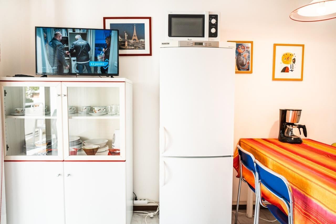 Una cucina compatta con forno a microonde, TV e frigorifero. Alle pareti, quadri incorniciati e un tavolo con una tovaglia colorata.
