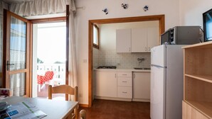 Cocina compacta con armarios blancos, un refrigerador y un microondas. Hay una mesa de comedor con sillas y una ventana con cortinas.