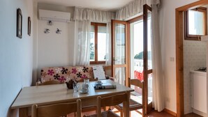 Un cuarto acogedor con una mesa de comedor de madera, sillas, un sofá con cojines estampados, un ventilador de techo y vistas al exterior a través de un ventanal amplio.
