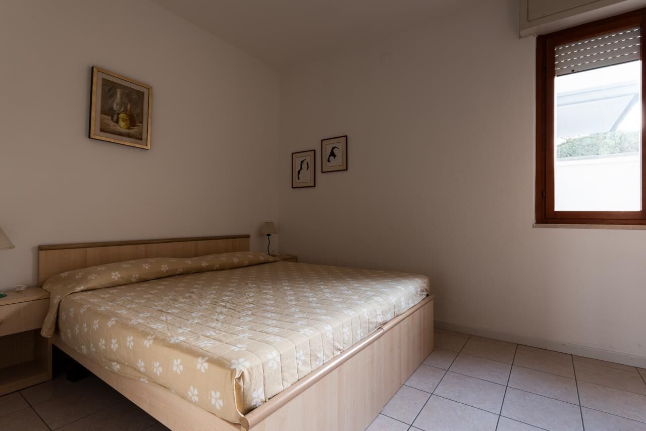 A bedroom with a bed, a nightstand, a window, and two framed pictures on the wall.