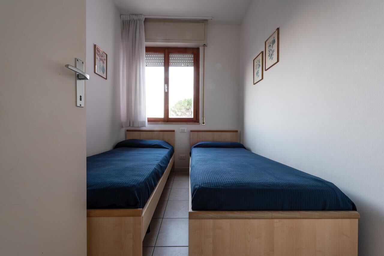 Un alojamiento pequeño, de una sola habitación, con dos camas de madera, una ventana con cortinas y una puerta con manija.