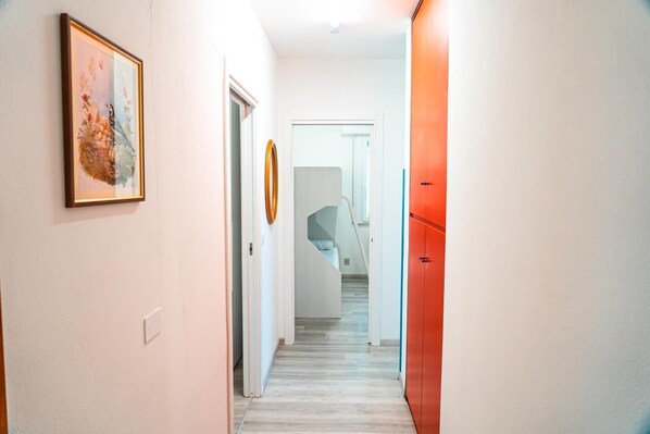 Un pasillo con una obra enmarcada a la izquierda, una puerta con un espejo circular y un armario rojo a la derecha.