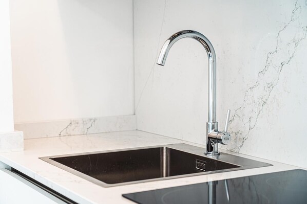Una cocina moderna con un elegante lavamanos de acero inoxidable, una placa de inducción negra y un salpicadero de mármol.