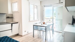 A bright, modern kitchen with white cabinets, a dining table with chairs, and a view of the sea through large windows.