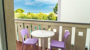 A balcony with a round table and two purple chairs, overlooking a beach and greenery.