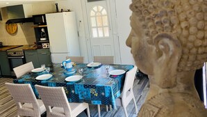 Comedor con una mesa preparada para cuatro personas, rodeado de sillas de mimbre. Un Buda está en primer plano.
