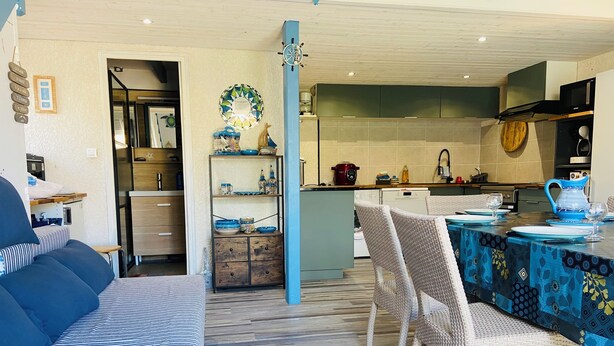 Una sala de estar acogedora con un sofá y sillones, un comedor con mesa y sillas, y una cocina con electrodomésticos modernos.
