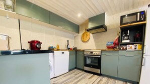 Cocina compacta con lavavajillas, horno, microondas y tabla de cortar de madera en la encimera.