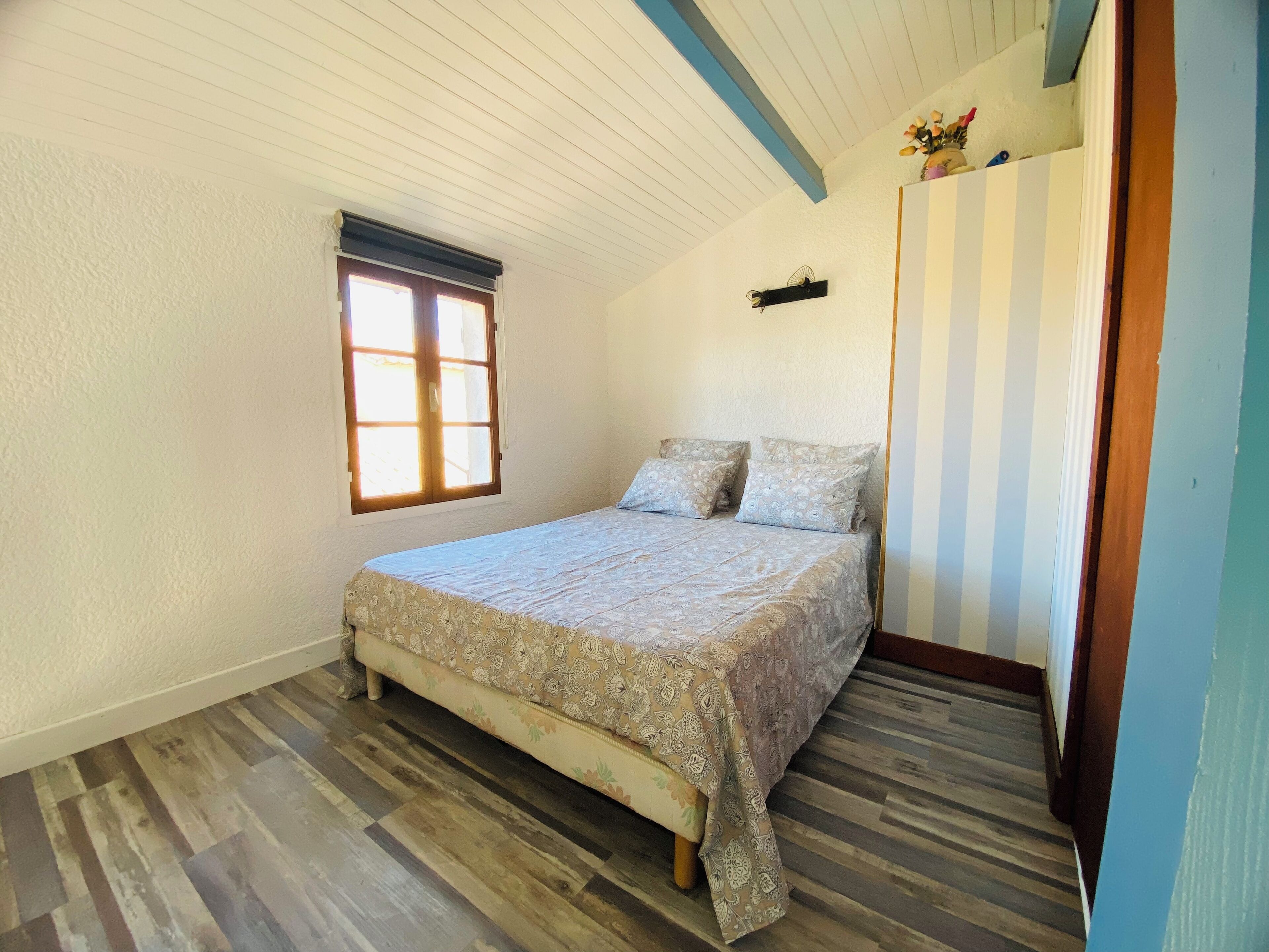 Een slaapkamer met een bed, een raam en een gestreepte muur.