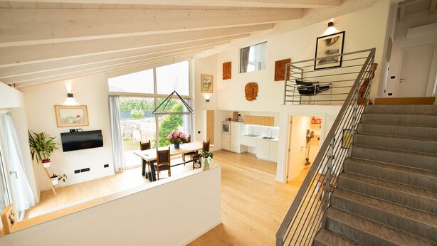 Un vaste espace de vie doté d’un plancher en bois, d’une table à manger avec des chaises, d’un coin cuisine et d’un escalier.
