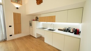 Une cuisine moderne avec des meubles blancs, un plancher en bois, un four encastré et un plan de travail équipé de divers appareils.