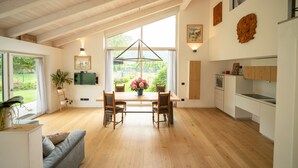 Une cuisine spacieuse avec un plancher en bois, un coin repas avec une table et des chaises, et une grande fenêtre donnant sur un paysage verdoyant.
