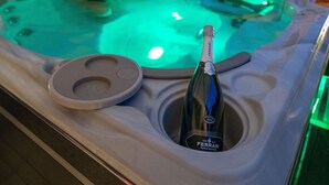 Un bain à remous avec une bouteille de vin Ferrari, entouré d’un espace extérieur aménagé avec une tente et une piscine.