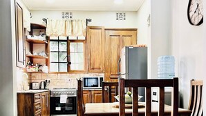 Una cucina con mobili in legno, un tavolo da pranzo con sedie, un frigorifero e un dispenser di acqua.