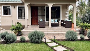 Una casa a due piani con un portico coperto, una porta d'ingresso e un piccolo giardino con piante in vaso e un vialetto.