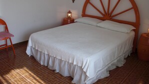 A bedroom with a wooden bed frame, white bedding, a nightstand with a lamp, and a chair. - TRIVANO PARCO ULIVI SECONDO PIANO (Cirella)