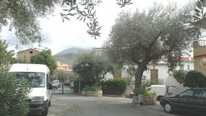 A residential street with parked cars, a white van, and a gated entrance. - TRIVANO PARCO ULIVI SECONDO PIANO (Cirella)
