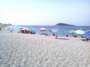 Ein Kiesstrand mit Sonnenschirmen und Personen.