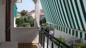 A balcony with a view of buildings and trees, a striped awning, and a tiled floor. - TRIVANO PARCO ULIVI SECONDO PIANO (Cirella)