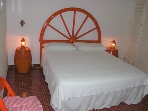 Ein Einzelbett mit Holz-Kopfteil, zwei Nachttischlampen und ein karierter Stuhl.