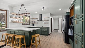 Een moderne keuken met een centraal eiland, houten krukken en groene keukenkastjes.