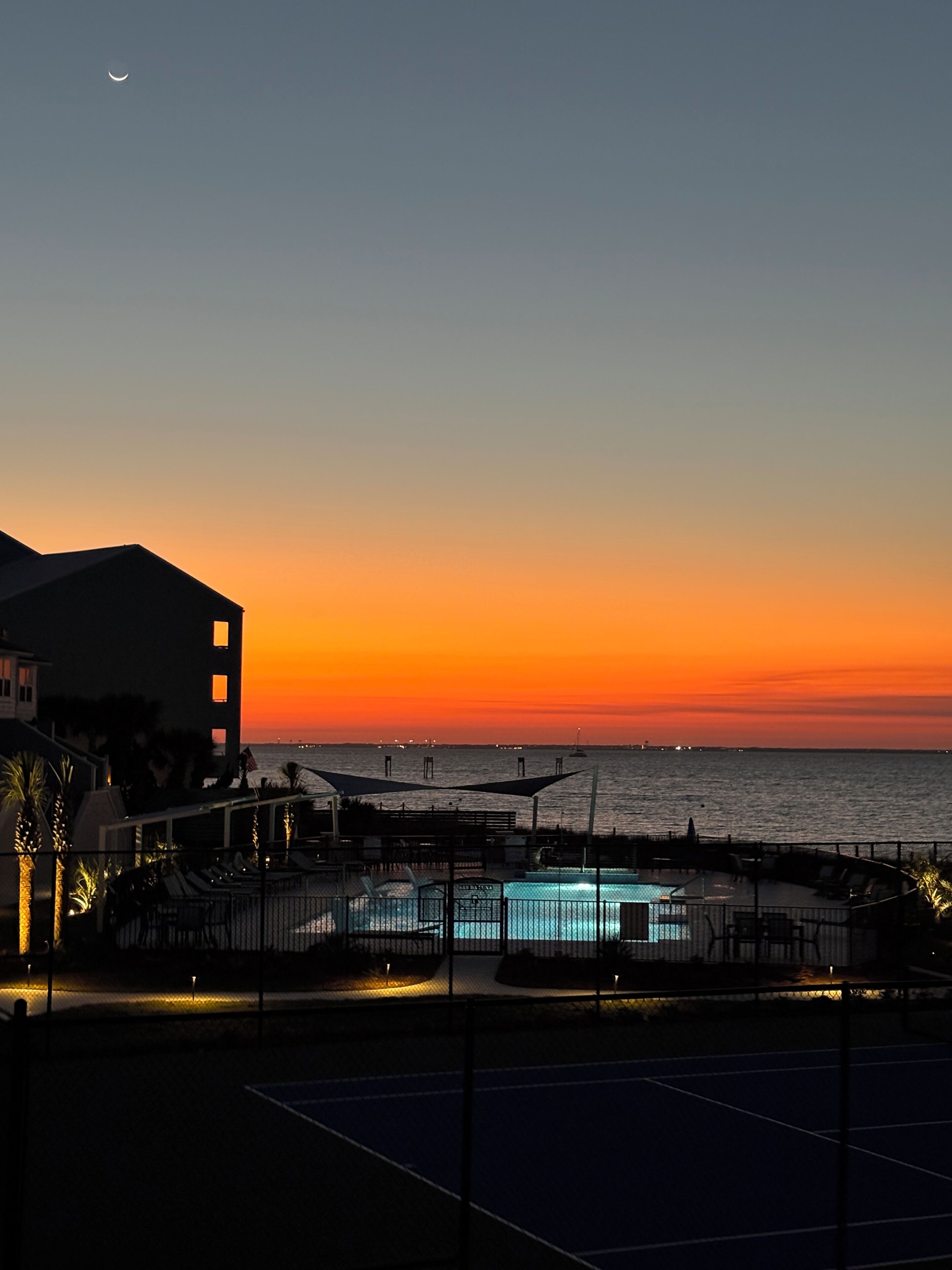 En vacker solnedgång sedd från en hotellbalkong med utsikt över en swimmingpool och havet.