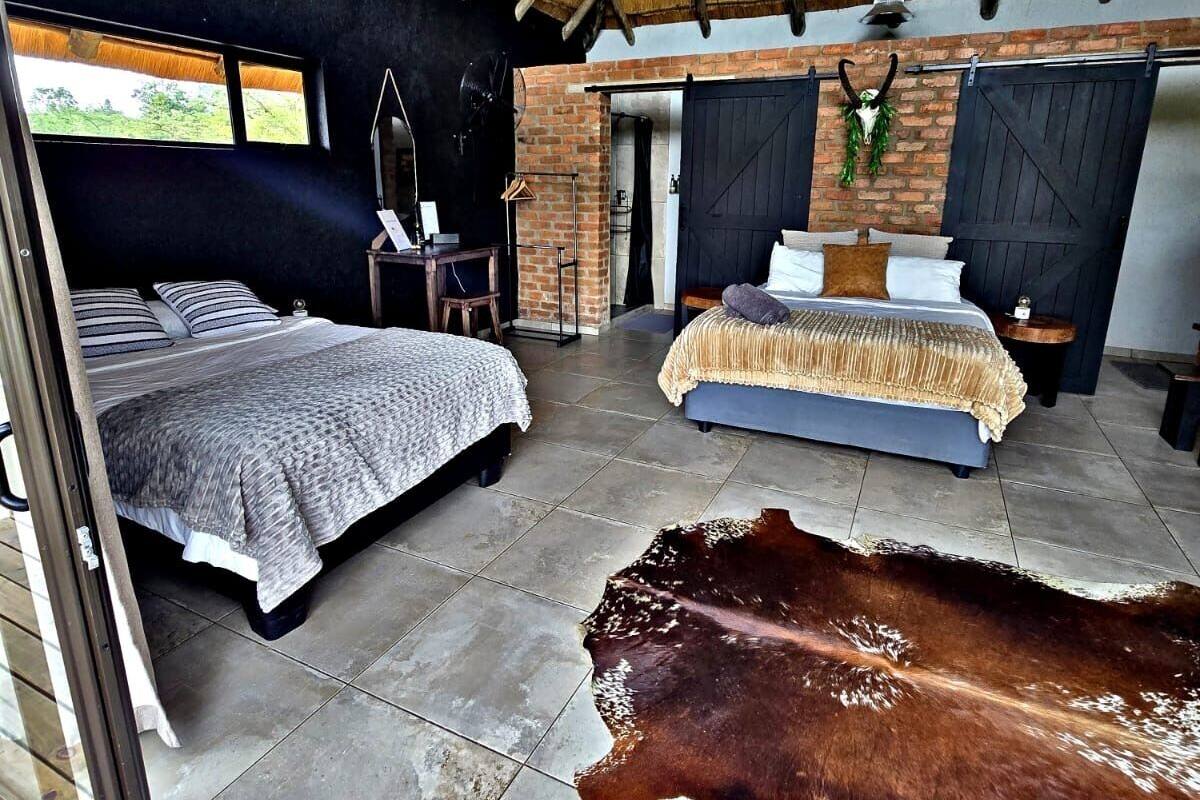 Amplia habitación con dos camas, un tapiz grande de cuero de vaca y una pared de ladrillo rústica.