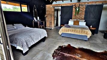 Amplia habitación con dos camas, un tapiz grande de cuero de vaca y una pared de ladrillo rústica.