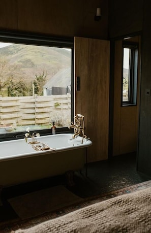 Un baño con una bañera independiente, una puerta de madera y vistas a un paisaje rural.